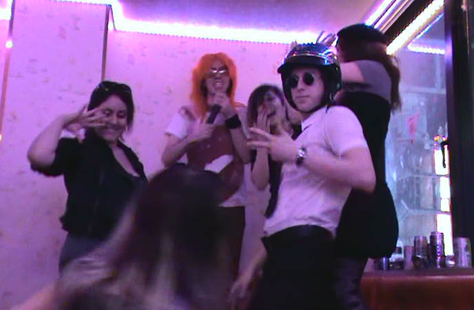 karaoke room with neon lights, silly singing songs in karaoke booth, FUNNY J-HORROR MOVIE. TOKYO GHOST STORY WITH DRAG QUEENS, COSPLAY & JAPANESE SCHOOLGIRLS, cross-dressing, goth fashion in Japan, DJ Sisen Tokyo Decadance, cute Swedish male model, transsexuals clothing and makeup